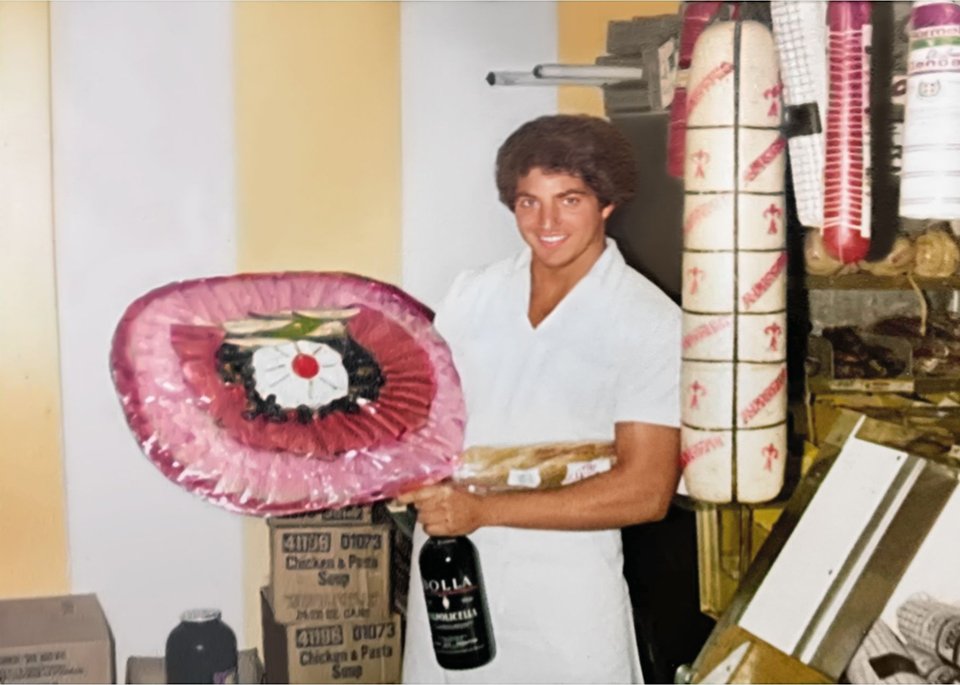 Thomas Rippy smiling while holding a deli meat tray and wine bottle in a meat shop