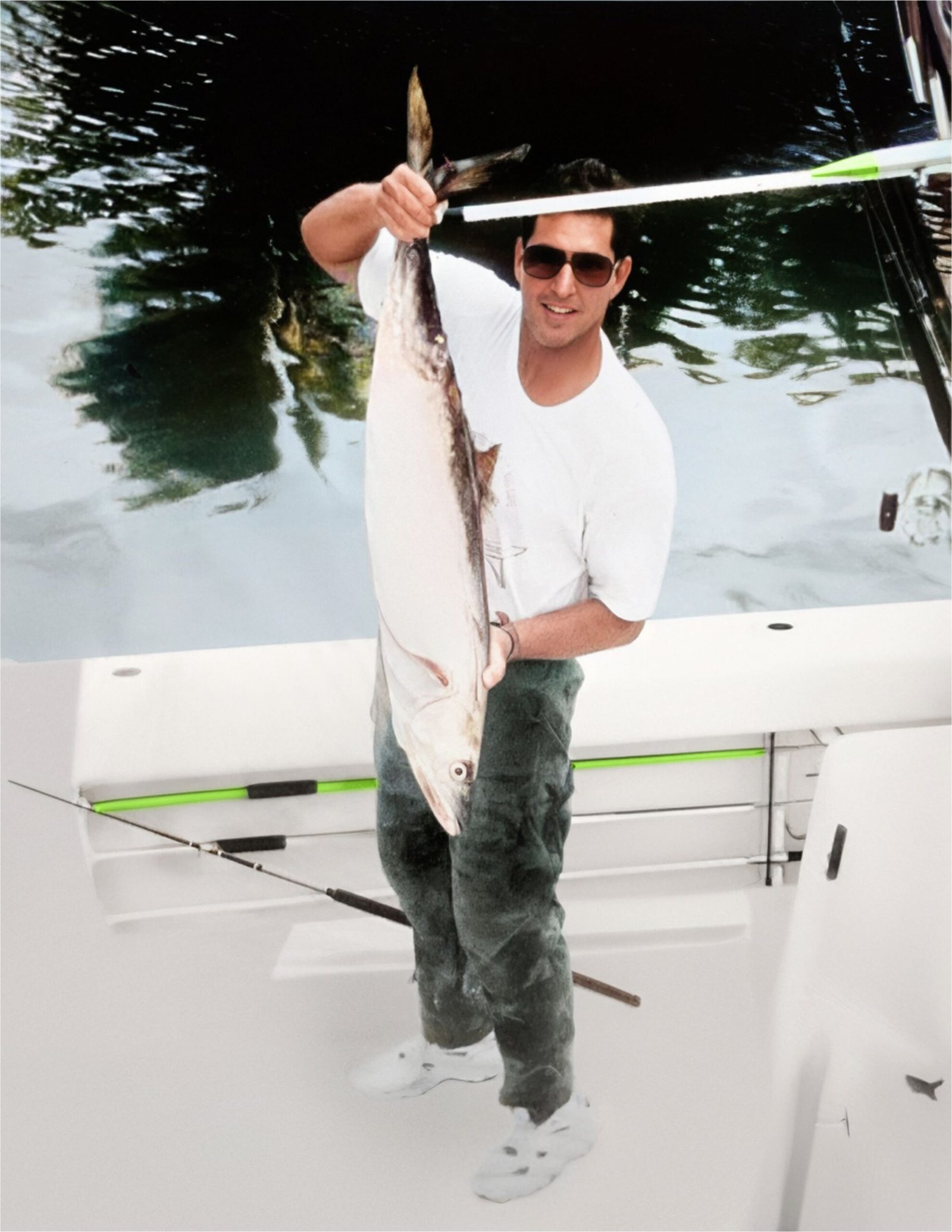 Thomas Rippy proudly holding a large fish on a boat during a fishing trip in Miami, 1980s, wearing sunglasses and a white t-shirt.